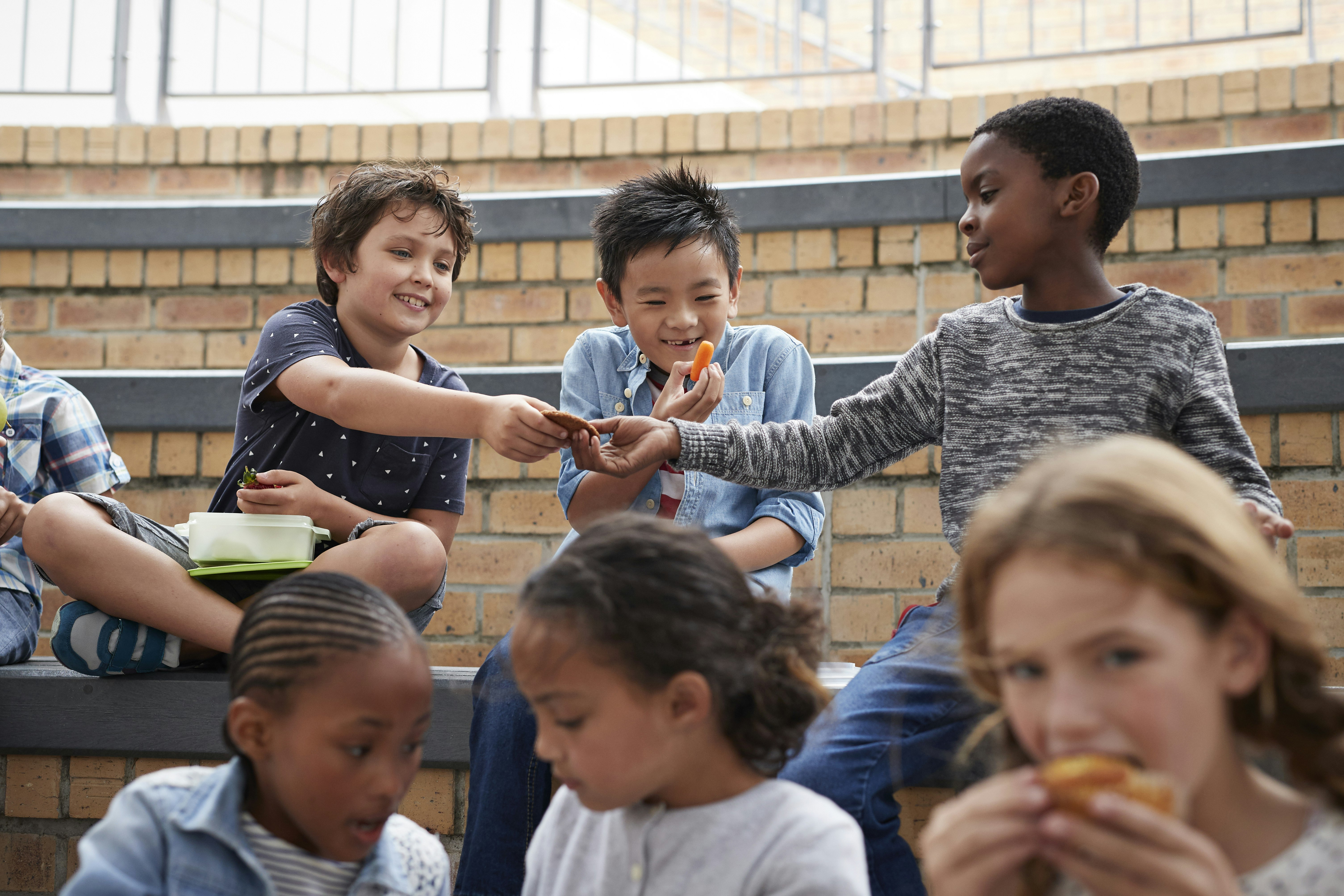 A group of children sitting together, laughing and eating lunch