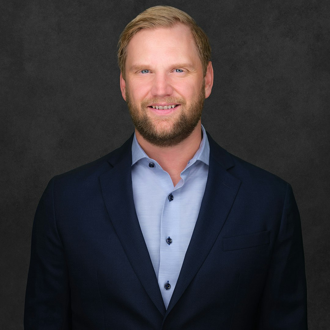 Gary McDonald smiling and wearing a suit and a blue shirt with the top button undone