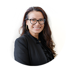Grace Dien standing side-on, wearing glasses and a suit, and smiling