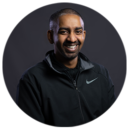 Thejus Swamy standing side-on, wearing a black zip-up hooded fleece and smiling